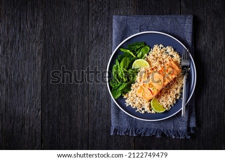 portion of Poached Salmon in Coconut Lime Sauce with brown rice and fresh spinach, salmon fish curry with rice and greens on a plate, view from above, flat lay, free space