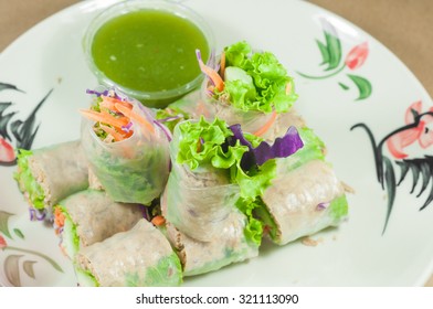 Portion of spring rolls on old wood with spicy sauce, vegetables and in noodle tube