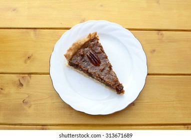 Portion of traditional pecan pie on a white plate on a wooden table