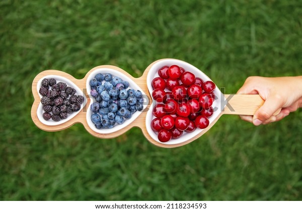 Portion wooden dish on green background top\
view,in a hand on the grass. Wooden partitioned dish divided into\
equal 3 section. Compartmentals dish for food, dessert, fruit,\
berries and vegetable.