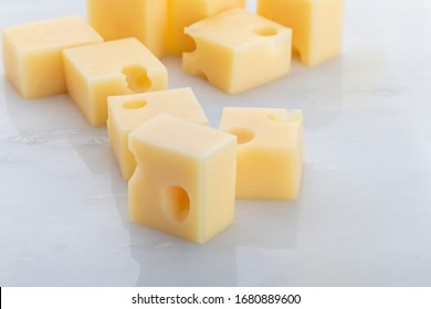 Portions (cubes, Dice) Of Emmental Swiss Cheese. Texture Of Holes And Alveoli. On White Marble Background.