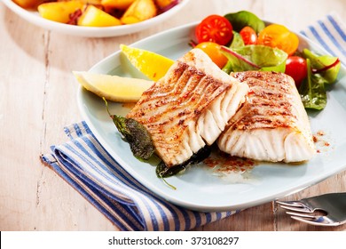 To portions of fresh grilled pollock or coalfish served with colorful salad and slices of lemon, close up high angle view
