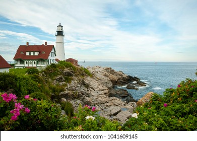 Portland Head lighthouse is surrounded by rocks, ocean, and beach roses on a warm summer day along the rocky coast in Maine. It is the oldest beacon in Maine.