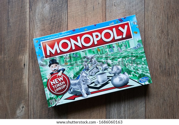 Portland, OR, USA - Mar 28, 2020: Top view of\
Monopoly board game box isolated on a wooden flooring background.\
The classic fast-dealing property trading board game is currently\
published by Hasbro.