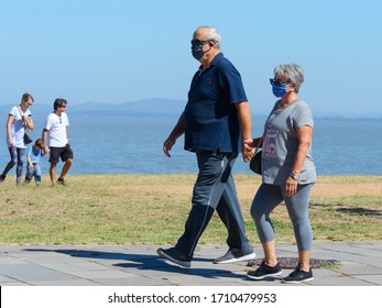 Porto Alegre / Brazil - April 21 2020: Old Couple Walking Outdoors Using Facial Masks During Coronavirus Quarantine Period. Out Of Focus Young Family Not Using Mask During COVID 19 Outbreak.