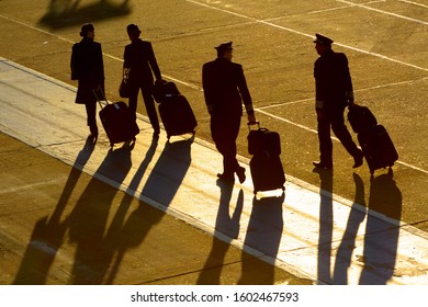 Porto Alegre / Brazil - October 04 2014: Flight Attendants And Pilots Walking With Bags. Professionals Of Aviation Including Cabin Crew And Pilot Silhouette Early In The Morning With Long Shades.