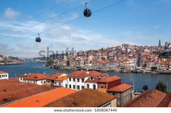 PORTO, PORTUGAL: Riverfront\
view with city red tile roofs, old wineries and cable cars in blue\
sky on 22 May, 2019. Portuguese language has 250 million total\
speakers