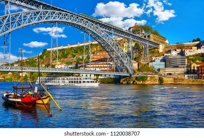 Porto, Portugal. View at Ponte de Dom Luis bridge on river Douro. Boats with barrels with port wine and pleasure boat on water.