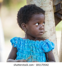 PORTO-NOVO, BENIN - MAR 8, 2012: Unidentified Beninese beautiful girl in a blue dress stays near the tree. People of Benin suffer of poverty due to the difficult economic situation.
