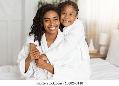 Portraif Of Beautiful Happy Black Mom And Daughter Posing On Bed In White Bathrobes, Hugging And Smiling At Camera, Loving African Mother And Child Enjoying Spending Time Together At Home, Free Space