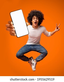 Portraif of excited African American teen guy jumping with smartphone, demonstrating empty screen on orange background, copy space for your mobile advertisement, mockup image - Shutterstock ID 1955629519