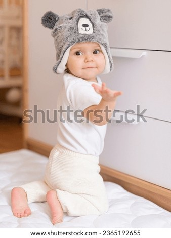 Portrait of 10 month old baby girl dressed in funny teddy hat is kneeling and smiling. Vertical orientation