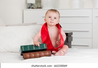 Portrait of 10 months baby boy in graduation ribbon looking at big books