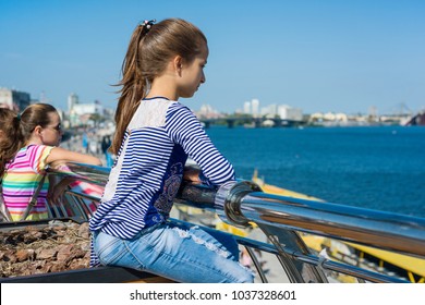 Portrait Of A 10 Year Old Girl In A Profile. Background Of A River In A Modern City, Blue Sky