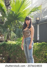 Portrait 20-25-year Girl Asian Woman With Long Black Hair Wearing Black Shirt, Blue Jeans, Acne Scars Faces, Standing In  Garden Tree. Spring Or Summer In The Evening Of The Day At Bangkok Thailand

