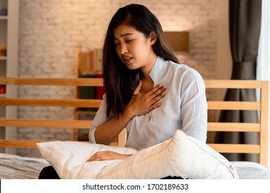 Portrait of 20s young Asian woman having difficulty breathing in bedroom at night. Shortness of breath, asthma, difficult to breathe problems. Corona Virus symptoms.