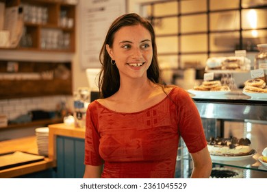 Portrait of a 25-year-old white woman with brown hair, waitress, working in a modern café pastry shop. Smiling and working. The place sells sweet cakes and coffee - Powered by Shutterstock