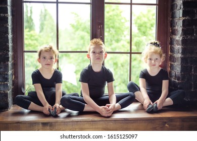 Portrait of 3 little children dancer two girls and one boy in black leotard sitting on window at dance studio. Recovery on dancing lesson. Kids hobby dancing. Active lifestyle in childhood.