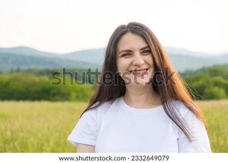 Portrait of a 30-year-old European woman smiling while looking at the camera while walking in nature in a field.