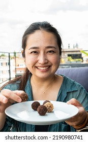 Portrait Of A 32 Year Old Japanese Woman Holding A Plate Of Round Chocolates, Belgium