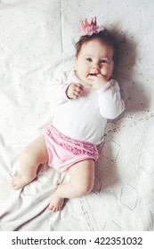 Portrait Of A 4 Month Cute Baby Girl Wearing Princess Crown Headband And Lying Down On A Bed With Polka Dot White Bedding, Top View