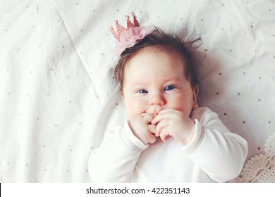 Portrait Of A 4 Month Cute Baby Girl Wearing Princess Crown Headband And Lying Down On A Bed With Polka Dot White Bedding, Top View