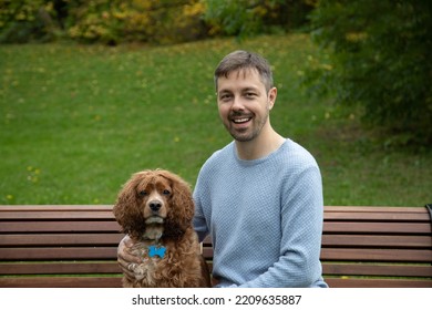 Portrait Of A 40 Year Old Caucasian Man Sitting On A Wooden Bench With His Cocker Spaniel Dog. The Man Is Wearing A Blue Shirt. This Photo Was Taken In The Autumn Months. 