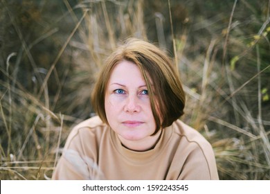 Portrait Of A 40 Years Old Woman Sitting On Dry Grass Outdoors