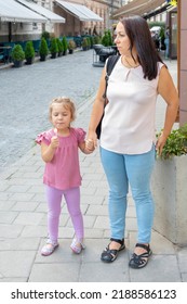 Portrait Of A 40-year-old Adult Woman And A Small 4-year-old Daughter On A Blurry Urban Background In Summer.Concept: Mom And Daughter Walking Around The Old Town, Tourism And Travel.