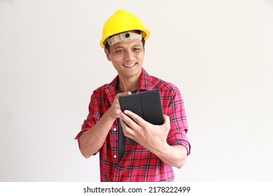 Portrait Of A 45 To 50 Year Old Asian  Man In Senior Engineer Concept. Wearing A Yellow Safety Helmet His Left Hand Held A Black Tablet. Looking At The Screen And Smiling. Isolated White Background.