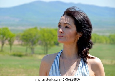 Portrait of 45 year old caucasian brunette woman looking away, with bare shoulders on a green field against the background of the mountains. Copy space