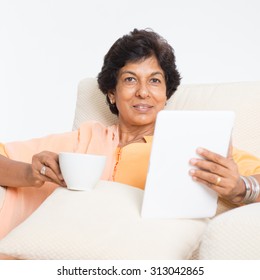 Portrait Of A 50s Indian Mature Woman Using Tablet Computer At Home. Older People, Modern Technology Concept. Indoor Senior People Living Lifestyle.