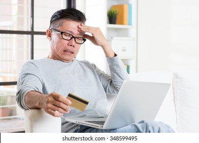 Portrait of 50s mature Asian man having problems while using computer internet doing online payment with credit card, sitting on sofa at home. - Shutterstock ID 348599495
