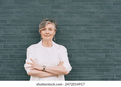 Portrait of 55 - 60 year old woman with grey hair, wearing white jacket, posing on grey background