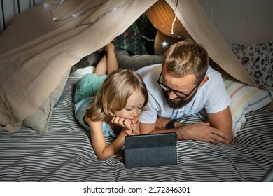 Portrait of a 6 year old boy and his father having fun playing in teepee tent. Father and son using digital tablet watching cartoons or playing computer games lying in kid tent at home.  - Powered by Shutterstock