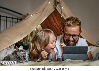 Portrait of a 6 year old boy and his father having fun playing in teepee tent. Father and son using digital tablet watching cartoons or playing computer games lying in kid tent at home.  - Powered by Shutterstock