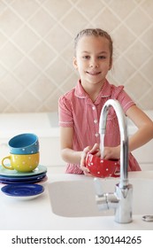 Portrait Of A 6 Years Old Girl Washing The Dishes At Home