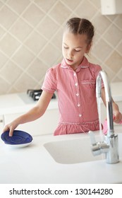 Portrait Of A 6 Years Old Girl Washing The Dishes At Home