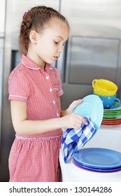 Portrait Of A 6 Years Old Girl Washing The Dishes At Home