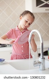 Portrait Of A 6 Years Old Girl Washing The Dishes At Home