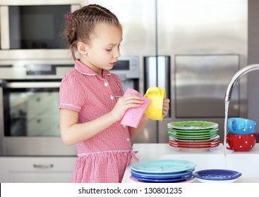 Portrait Of A 6 Years Old Girl Washing The Dishes At Home