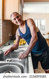 Portrait Of 60 Years Old Person Cleaning Fish Standing At Kitchen Sink At His House. Side View.