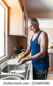 Portrait Of 60 Years Old Smiling Person Cleaning Fish Standing At Kitchen Sink Next To Window At His House