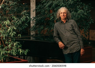 portrait of 65-year-old mature man at piano musical instrument in lobby of hotel gray curly hair, charismatic appearance. 