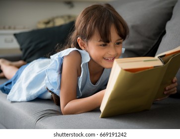 Portrait Of 7 Years Old Child Reading Book At Home,little Cute Girl Reading A Book And Siting On The Sofa,