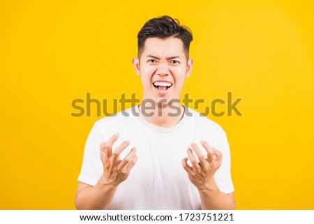 Portrait Aaian handsome young man standing wearing white t-shirt he expressions irate, angry face screaming, studio shot isolated yellow background