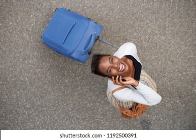 Portrait from above of happy african american woman walking with suitcase and mobile phone