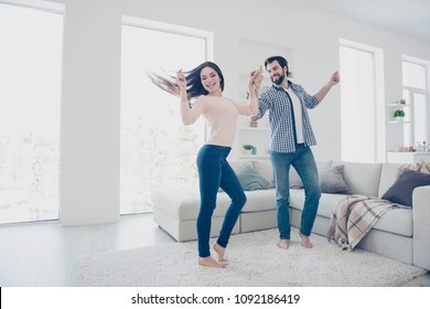 Portrait of active cheerful couple in casual outfits dancing singing indoor, in modern open space living room enjoying time together - Powered by Shutterstock