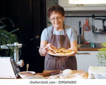 Portrait of an active elderly woman cooking in the kitchen. Grandma has prepared delicious pastries and is holding a plate of whites. Healthy homemade food.