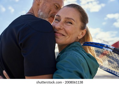 Portrait of active mature couple looking happy while embracing each other outdoors, ready for morning workout on tennis court - Powered by Shutterstock